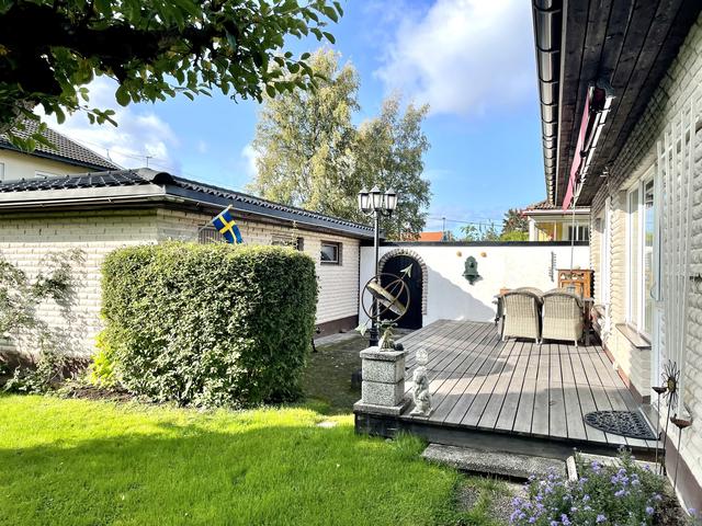 Trädäckad uteplats med markis, anslutande garage med förråd samt port mot infart och entrésida.