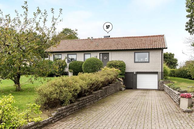 Välkomnande entrésida med garage i direkt anslutning och prydligt stenlagd uppfart