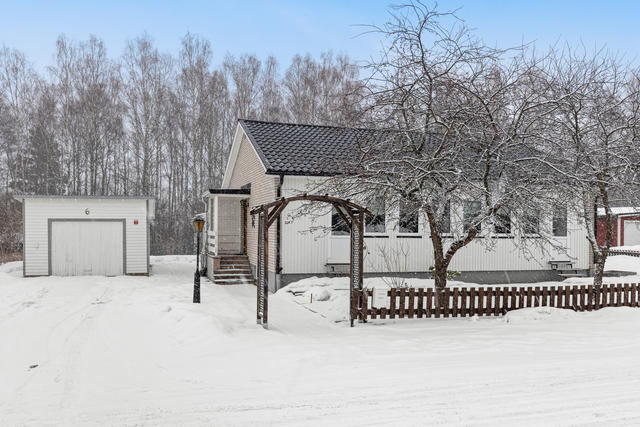 Fasad i väster med entré från husets norra gavel. Samt uppfart till huset med parkeringsplats och ett fristående garage. 