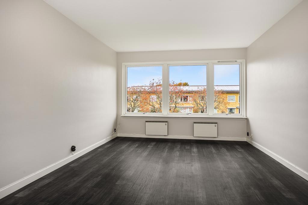 Bostadens vardagsrum är generöst till sin yta och har fint ljusinsläpp från fönsterna längst rummets ena kortsida.