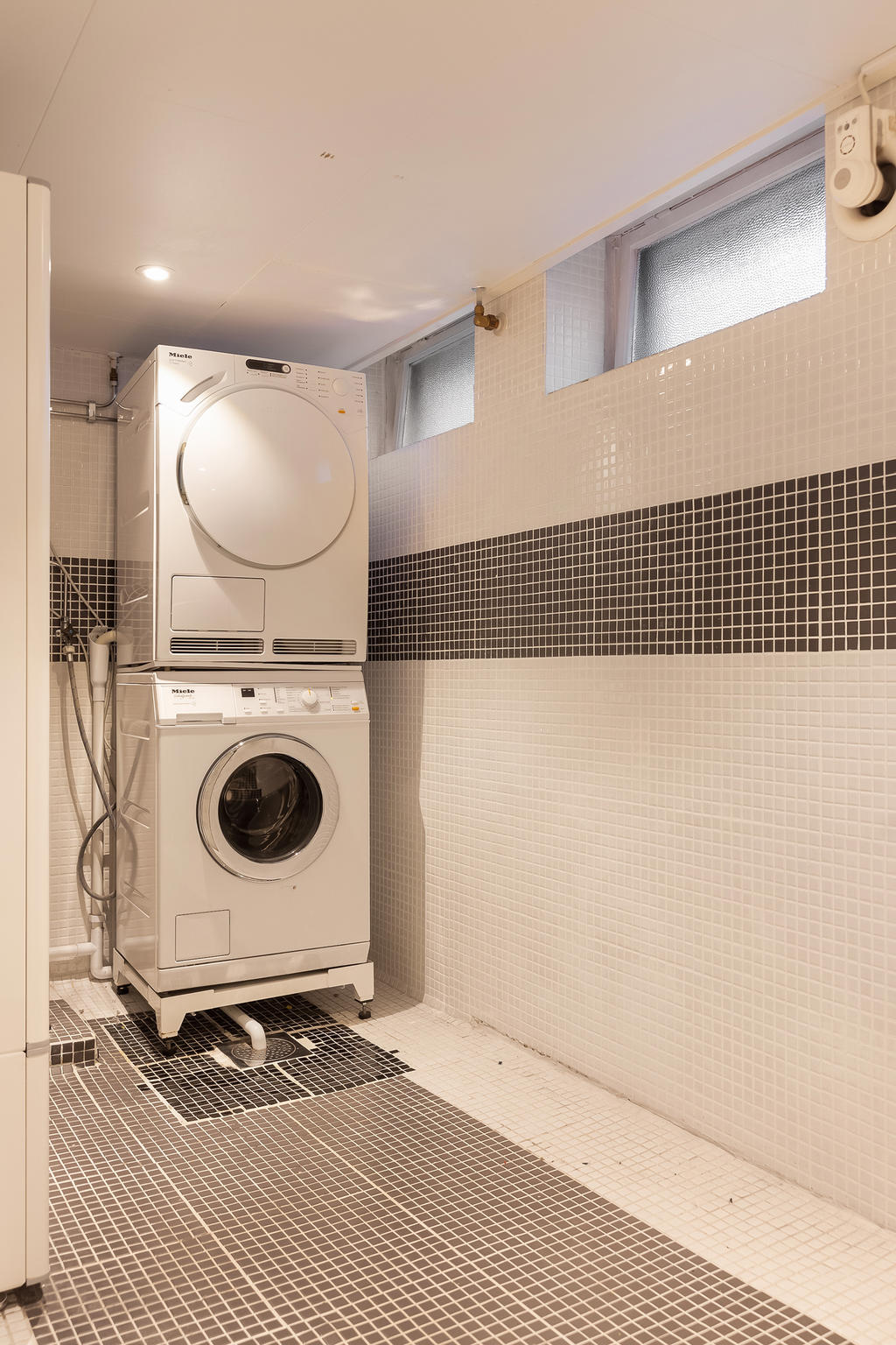 Tvättstuga med tvättmaskin och torktumlare från Miele och diskho till vänster om tvättpelaren