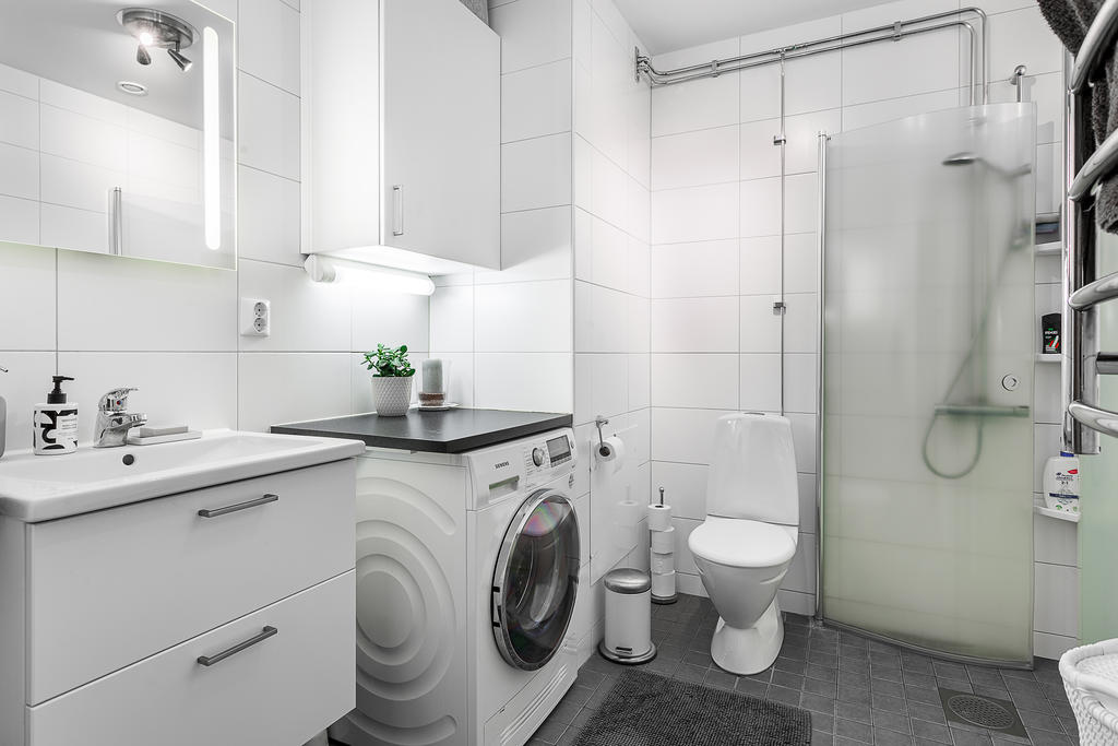 Bostadens badrum utrustat med tvättmaskin och duschväggar.