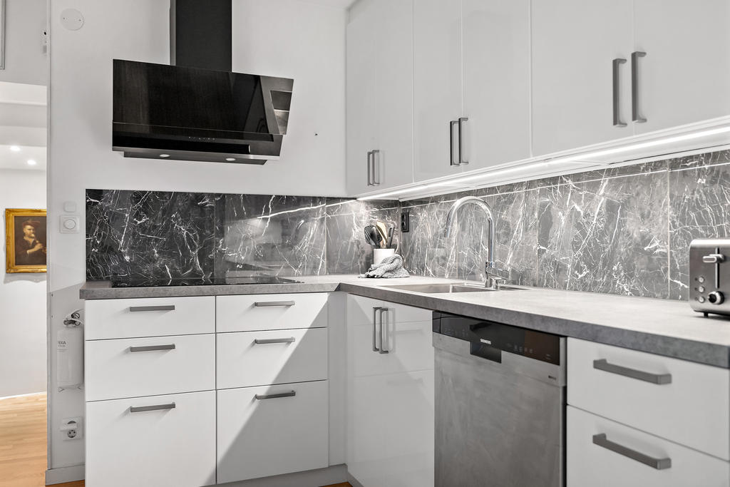 Modern stil med släta luckor, grå bänkskiva och marmorerade klinkerplattor. 