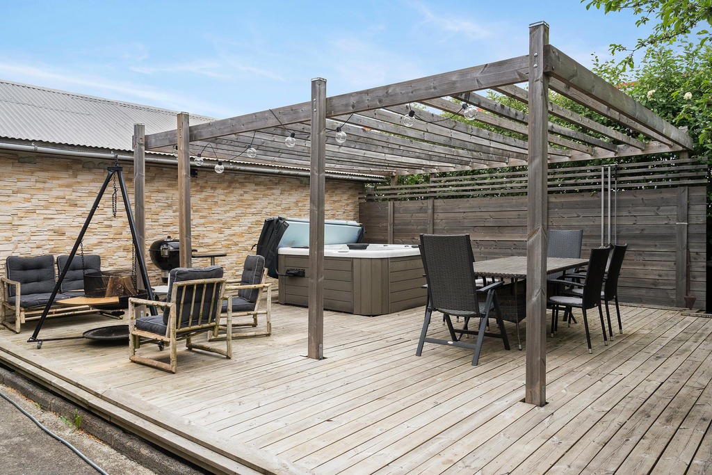 Sommarbild på trädäck med pergola, utekök och spabad
