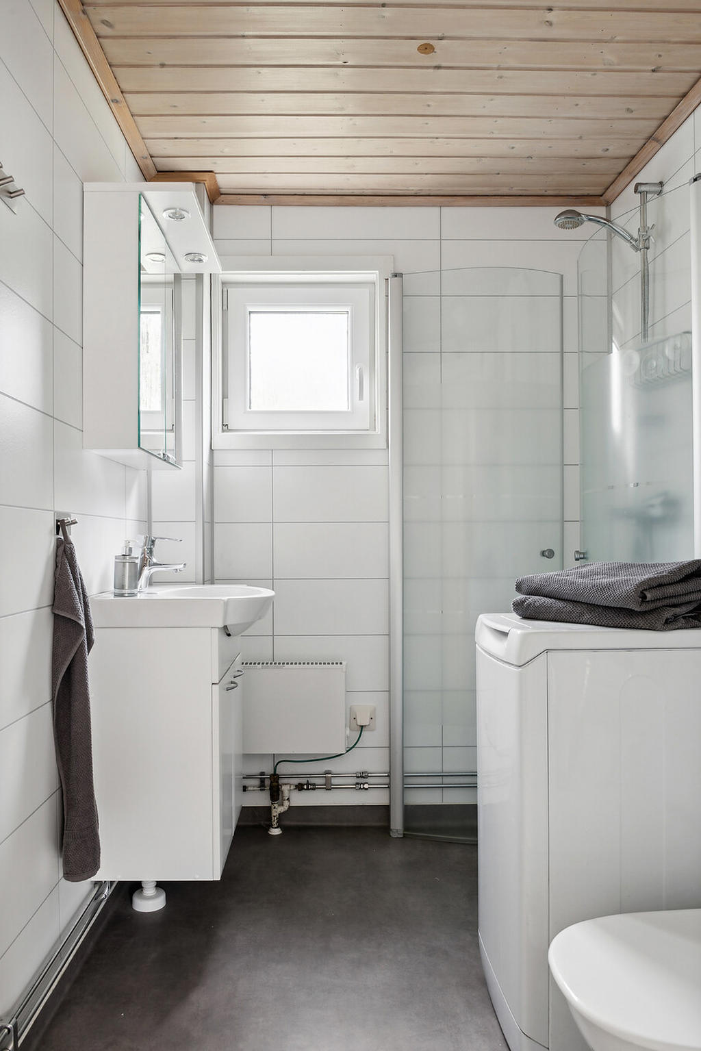 Badrummet är fräscht och modernt. Här finns det dusch, en praktisk tvättmaskin samt en stilren kommod med handfat och spegel. Ett perfekt utrymme för avkoppling och personlig vård.