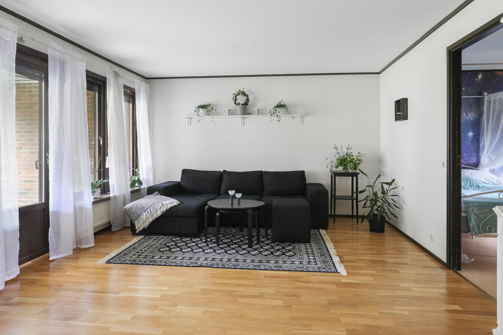 Ljust vardagsrum med parkettgolv, här når du uteplatsen på framsidan som är skyddad under tak.