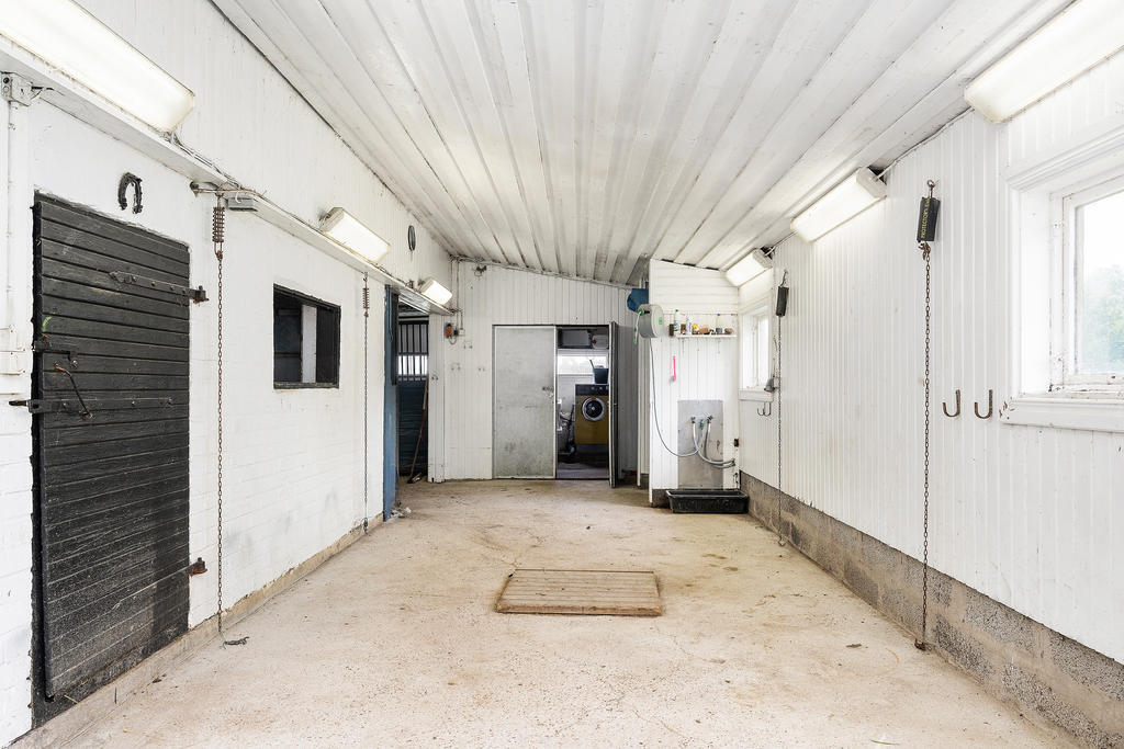 Stallgång med tvättstuga längst in. Till vänster ingång till höloft och längre ner stall/boxar.
