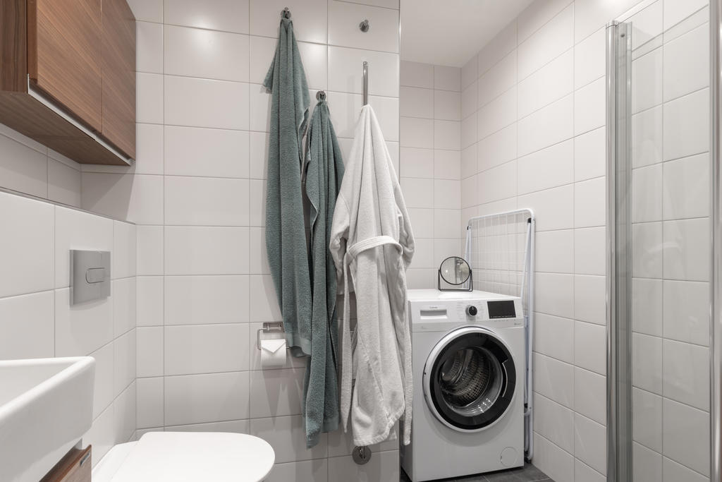 Helkaklat och klinkat badrum med tvättmaskin, dusch, wc och förvaring.