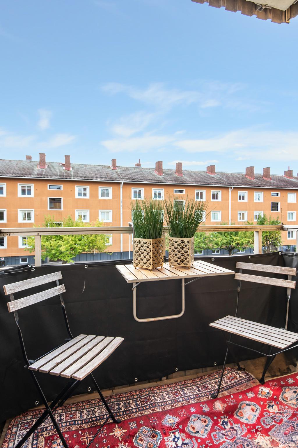 Balkong med utsikt mot en innergård med solläge. 