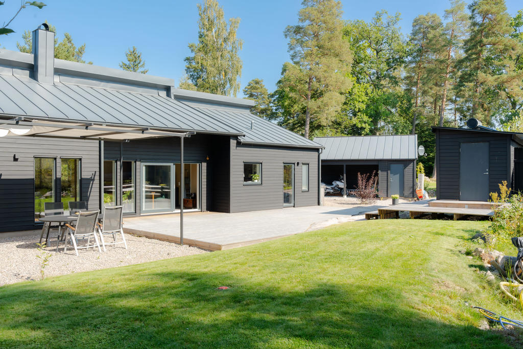 Baksida med trädäck, paviljong, gräsmatta och bastu.