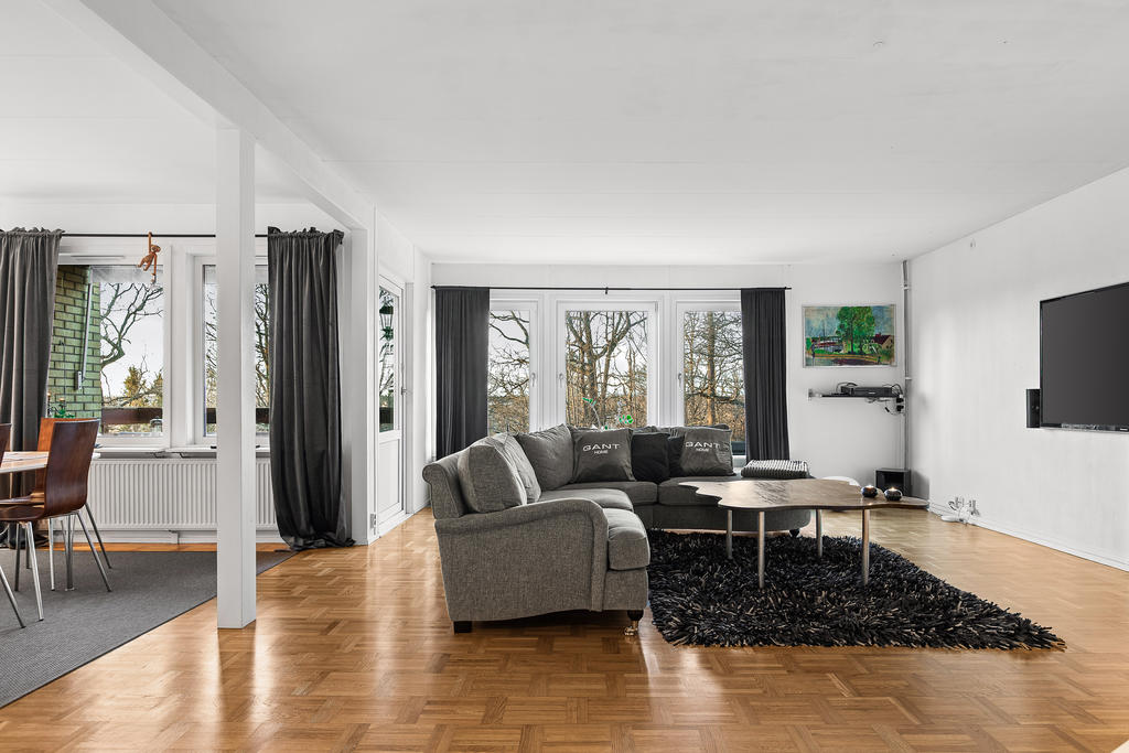 Vardagsrum med stora fönsterpartier och utgång till balkong