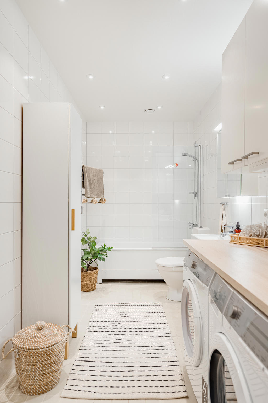 Rymligt badrum utrustat med wc, handfat, badkar, tvättmaskin och torktumlare med arbetsbänk samt badrumsskåp.