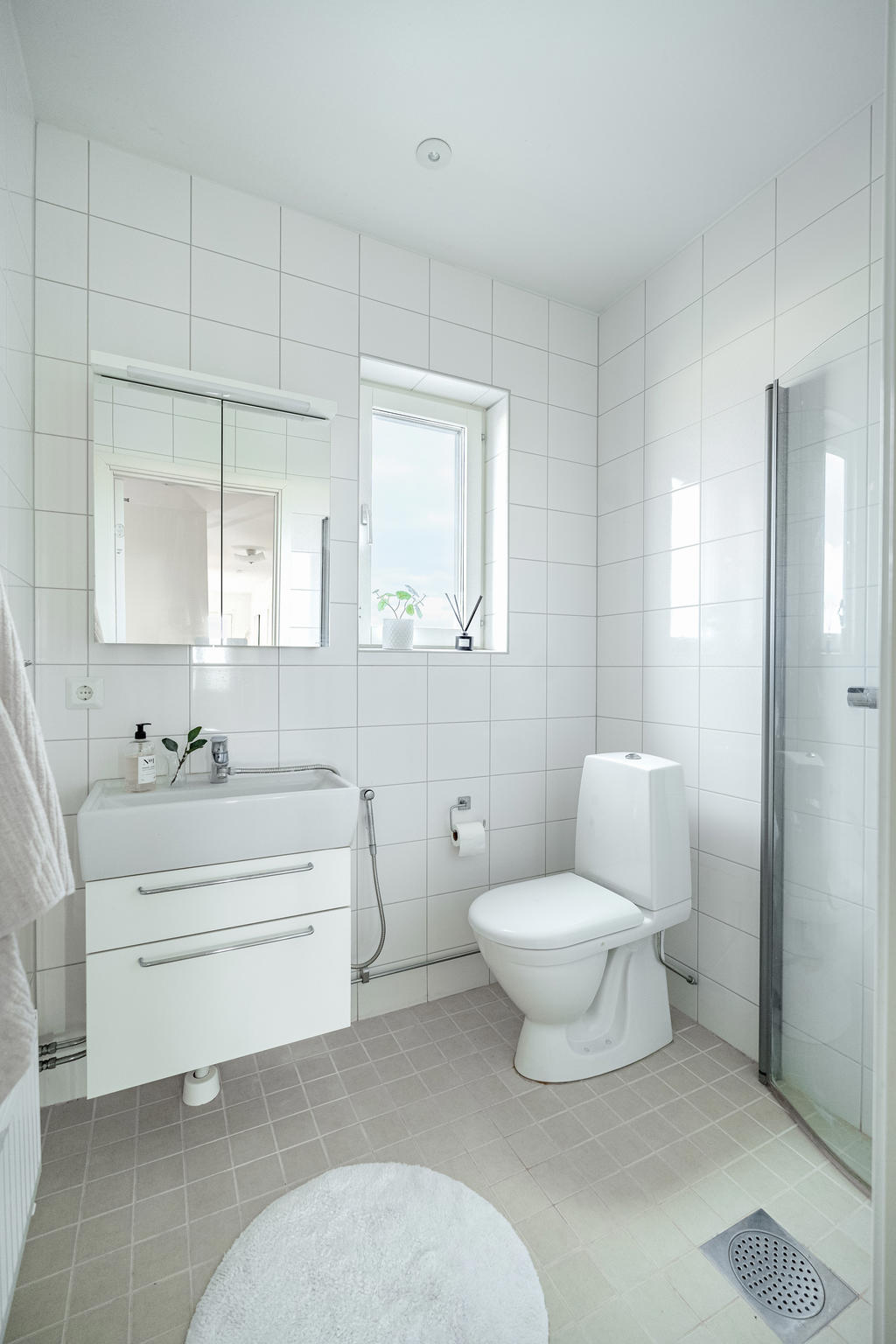 Badrum med fönster, utrustat med wc, handfat, dusch och baddrumsskåp.