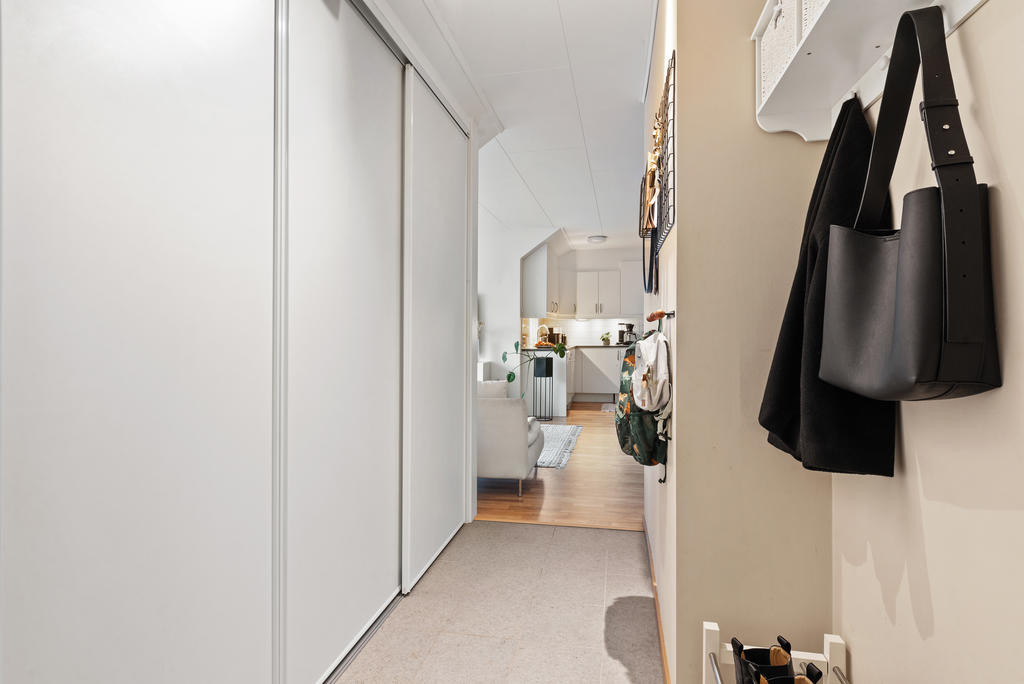Säkerhetsdörr till välkomnande hall med skjutdörrsgarderob direkt till vänster. Bra yta för ytterkläder till höger. Snyggt stengolv och ljust målade väggar.
