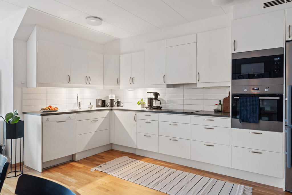 Generöst kök med bra arbetsytor för mat och bak. Vita luckor och lådförstycken, liggande kakel som stänkskydd, arbetsbänkar med mörk laminatskiva. Vitvaror från Electrolux från 2017.