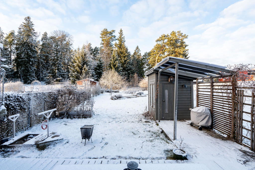 Husets baksida med altan och lättskött mindre tomt mot skogsparti.