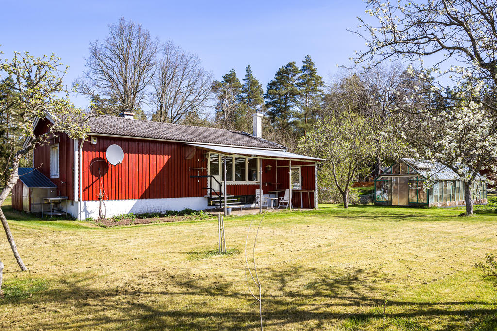 Bostadens baksida med två växthus till höger i bild.