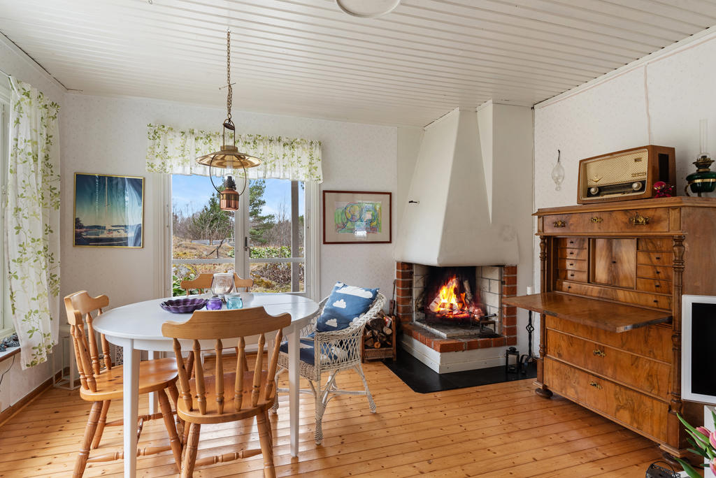 Generöst vardagsrum med stora fönster i tre väderstreck. En härlig öppen spis att mysa framför och utgång mot altanen i väster. Ljusa väggar med tapet i diskret mönster, vitt tak och det vackra trägolvet.