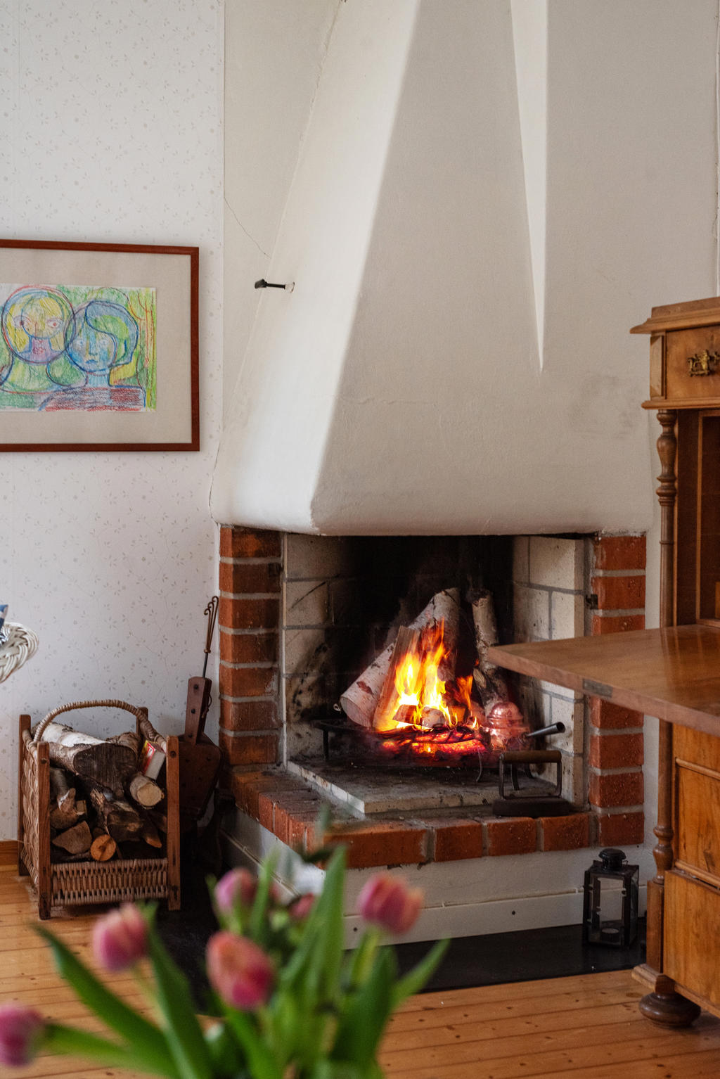 Generöst vardagsrum med stora fönster i tre väderstreck. En härlig öppen spis att mysa framför och utgång mot altanen i väster. Ljusa väggar med tapet i diskret mönster, vitt tak och det vackra trägolvet.