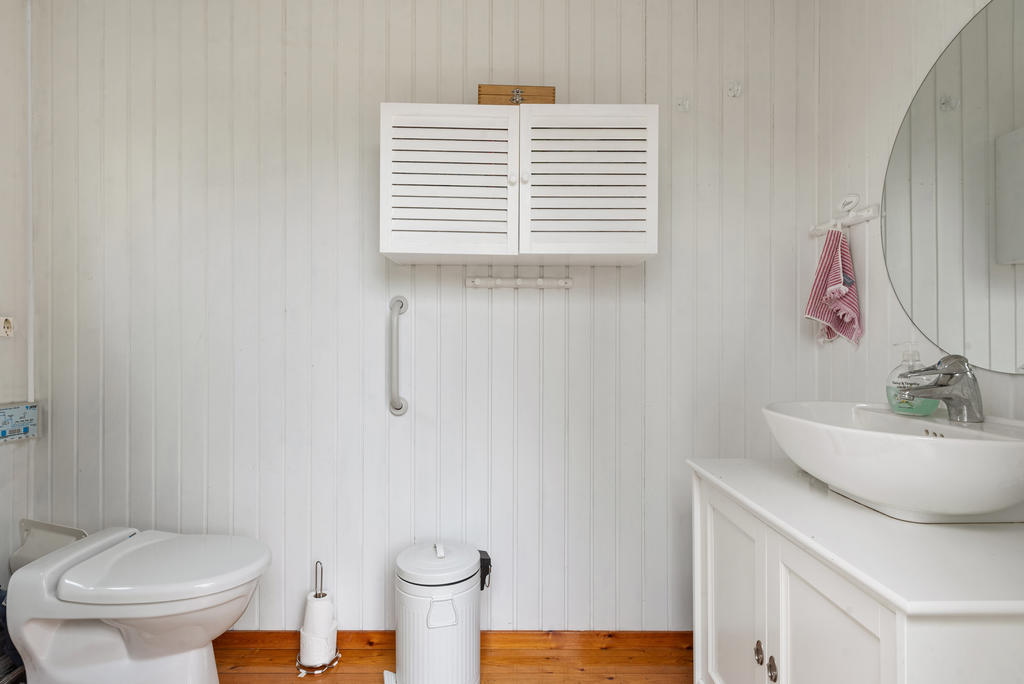 Med ingång från altanen hittar du badrummet där det finns en wc, duschkabin och handfat med kommod inunder. Även förvaringsskåp. Vit panel på väggarna och trägolv. 