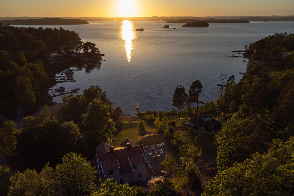 Flygfoto med bostaden vänd mot sjö och kvällssol.