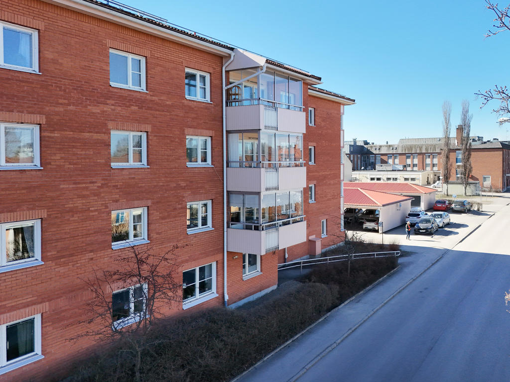 Vy över fasad i öst längs Långnäsvägen och föreningens p-plats med carport/garage. 