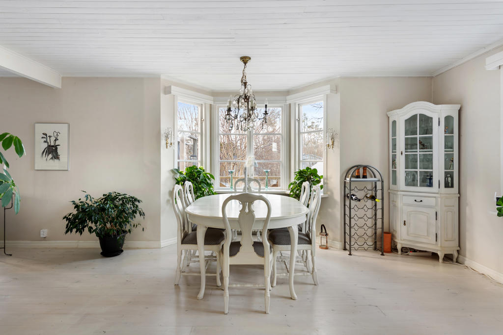 Efter hallen kommer ett jättestort rum där man idag börjar med en matsalsdel med plats för många gäster. Här har huset ett vackert burspråk ut mot väster och altanen. Ljusa väggar, fönster mot norr och väster, vitpigmenterat golv och vitt tak.