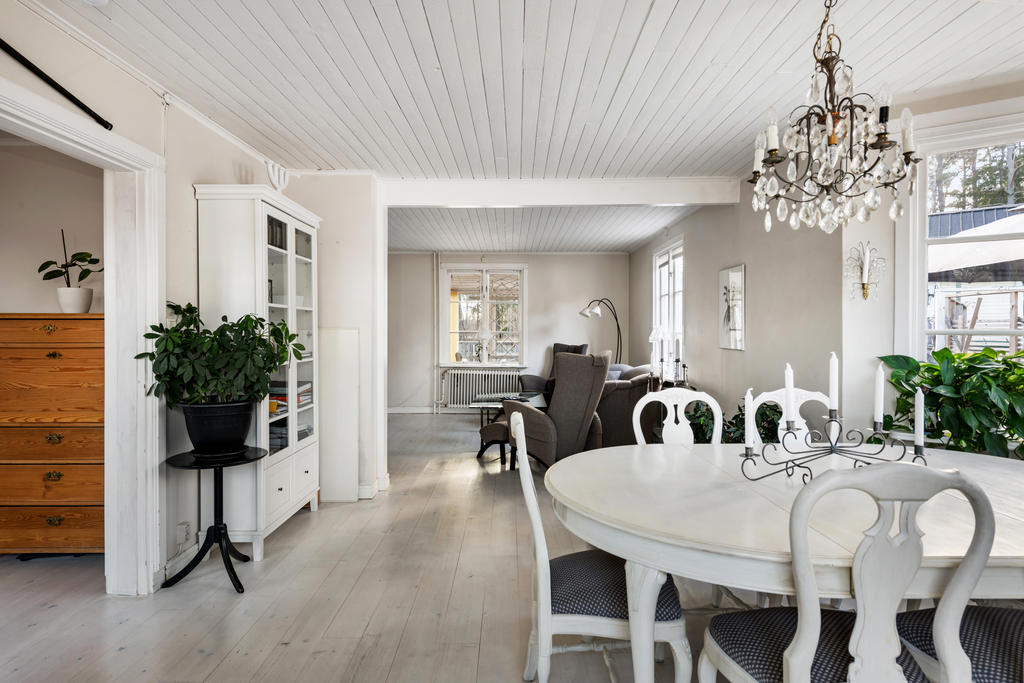Efter hallen kommer ett jättestort rum där man idag börjar med en matsalsdel med plats för många gäster. Här har huset ett vackert burspråk ut mot väster och altanen. Ljusa väggar, fönster mot norr och väster, vitpigmenterat golv och vitt tak.