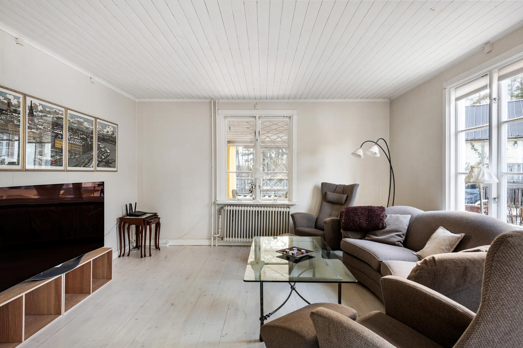 Matsalen följs direkt av ett sällskapsrum med plats för en stor soffa med tillbehör. Rummet hänger ihop med matsalsdelen och har vita väggar, fönster mot uterummet i söder och mot altanen i väster. Vitpigmenterat golv och vitt tak. 