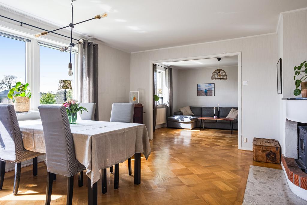 Rymligt och ljust vardagsrum med stora fönster som släpper in rikligt med dagsljus. Här finns plats för både soffgrupp och matbord. Rummet har vackert parkettgolv och en hemtrevlig eldstad som ger extra mysfaktor.