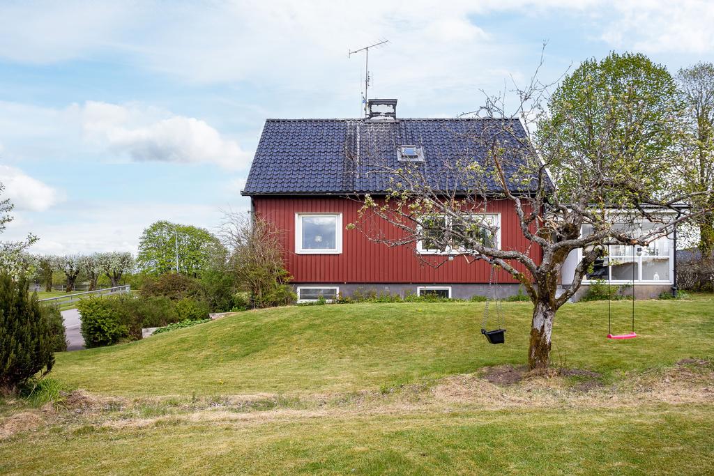 Charmig röd villa med svart tak, omgiven av härlig grönska.