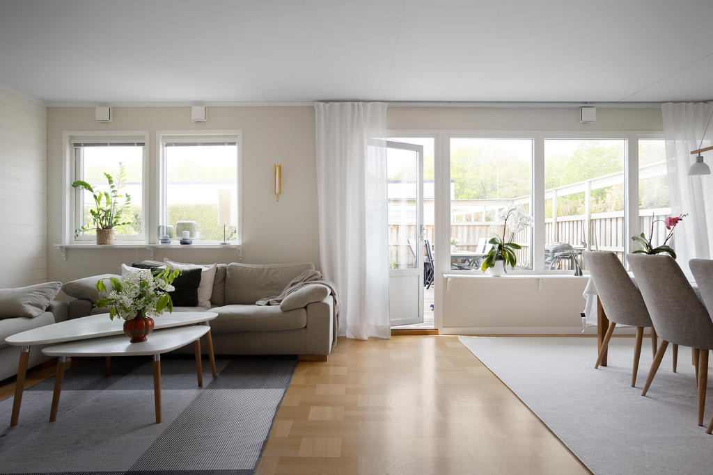 Ljust och trivsamt vardagsrum med stora fönsterpartier och utgång till den trevliga trädgården