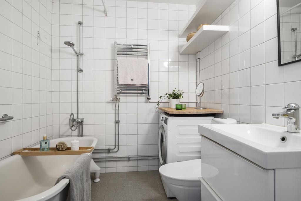 Helkaklat badrum med klinker på golvet.  Tvättmaskin med praktisk arbetsyta. Toa och handfat med kommod är av ny standard 