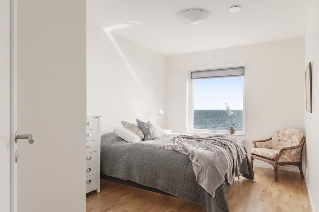Det större sovrummet är rofyllt och ljust med ekparkett och vitmålade väggar. Här vaknar du till en fantastisk havsutsikt.