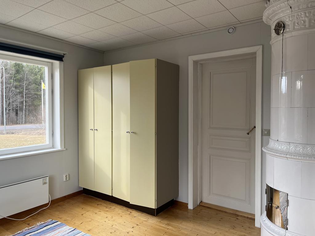 Säljarens bild på sovrum innanför kök med kakelugn och nymålade garderobsdörrar. 