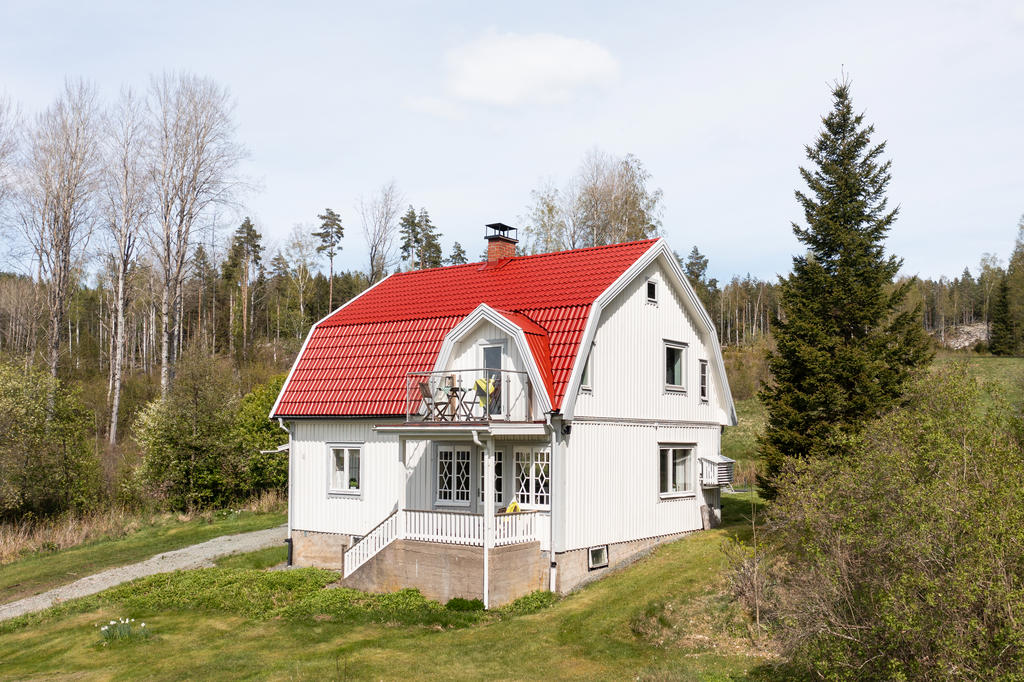 Veranda under tak och balkong med glasräcke på ovanvåning.