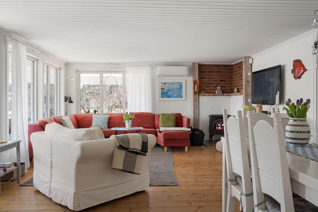 Öppen planlösning för hall, vardagsrum och matplats. Rummet är rymligt med många stora fönster och här finns en värmande kamin som är i bruk.