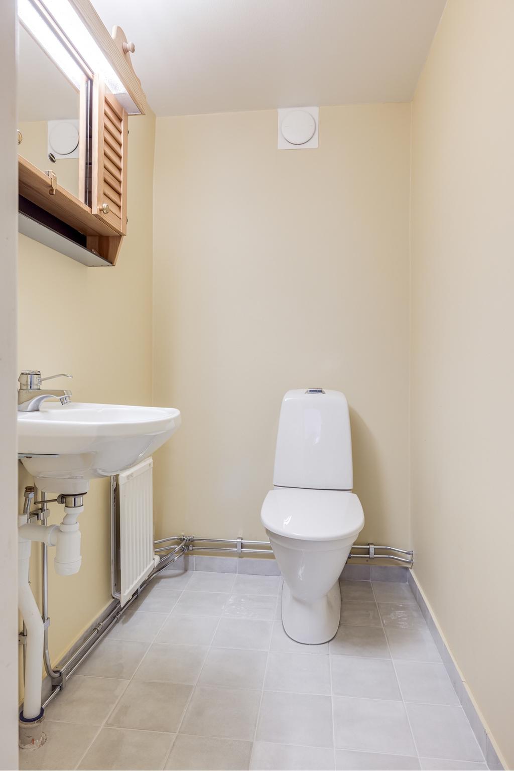 Den nyrenoverade toalettten med ljusgrått klinkers och en ljusgul varm ton på väggarna.