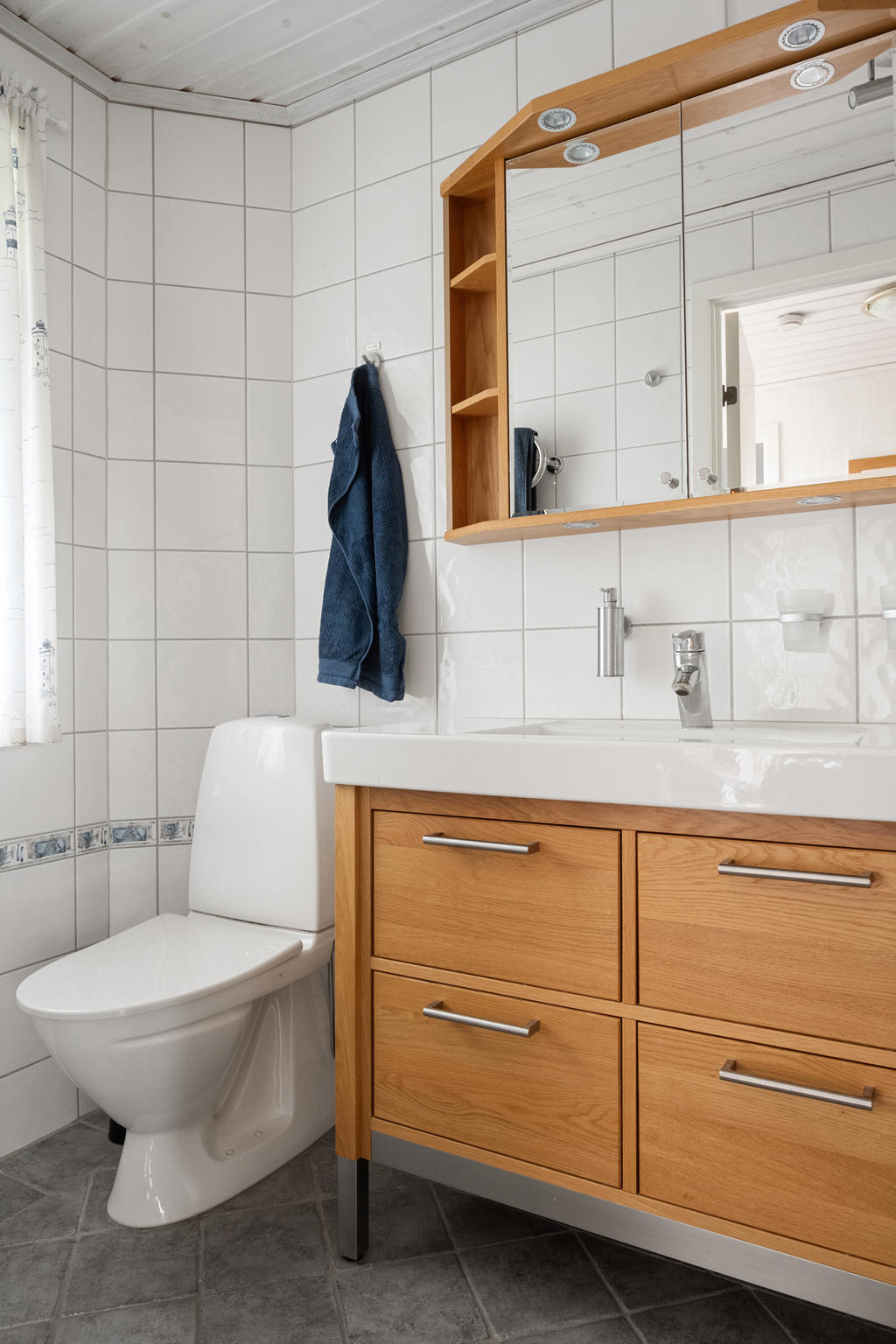 Helkaklat badrum med stilren dusch, wc och handfat. En praktisk kommod kompletterar spegeln, vilket ger både funktionalitet och elegans i detta välutrustade rum för dagliga rutiner.
