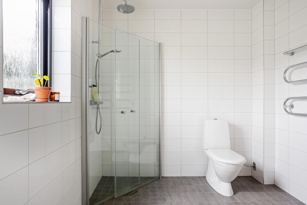 Direkt till vänster om hallen ligger det första av bostadens två badrum. Ett rymligt, helkaklat badrum med stilrent vitt kakel på väggarna och grå klinker på golvet. 