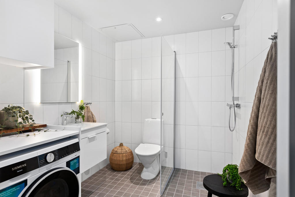 Helkaklat badrum i ljusa färger, med kombinerad tvättmaskin/torktumlare.