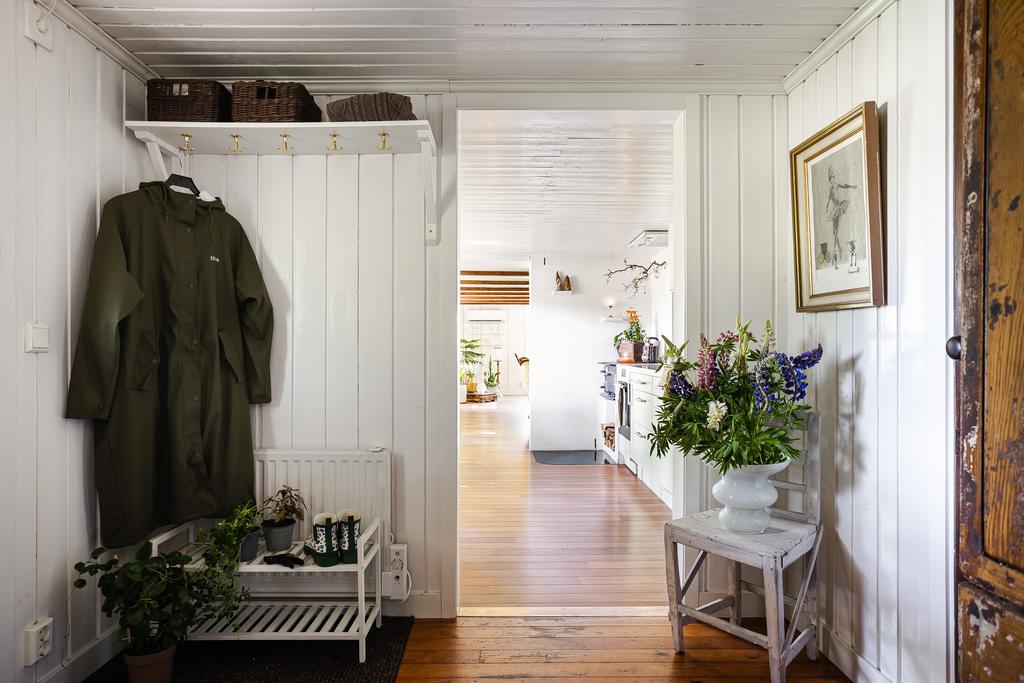 En ljus och välkomnande hall med vitmålade väggar och trägolv. Plats för avhängning samt dekorativa inslag som spegel och en charmig gammal dörr skapar en hemtrevlig känsla direkt vid ankomst.

