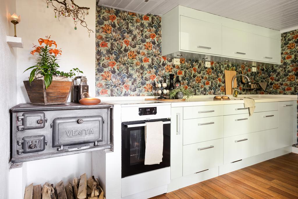 Ett stilrent och charmigt kök där modern funktion möter lantlig elegans. Ljusa skåpsluckor kombineras med en livfull, blommig tapet som ger rummet karaktär. Ett gammaldags vedspis ger en nostalgisk touch, medan fönstret släpper in rikligt med ljus. Köket har bra arbetsyta och förvaring, och det finns plats för en matgrupp vid fönstret.