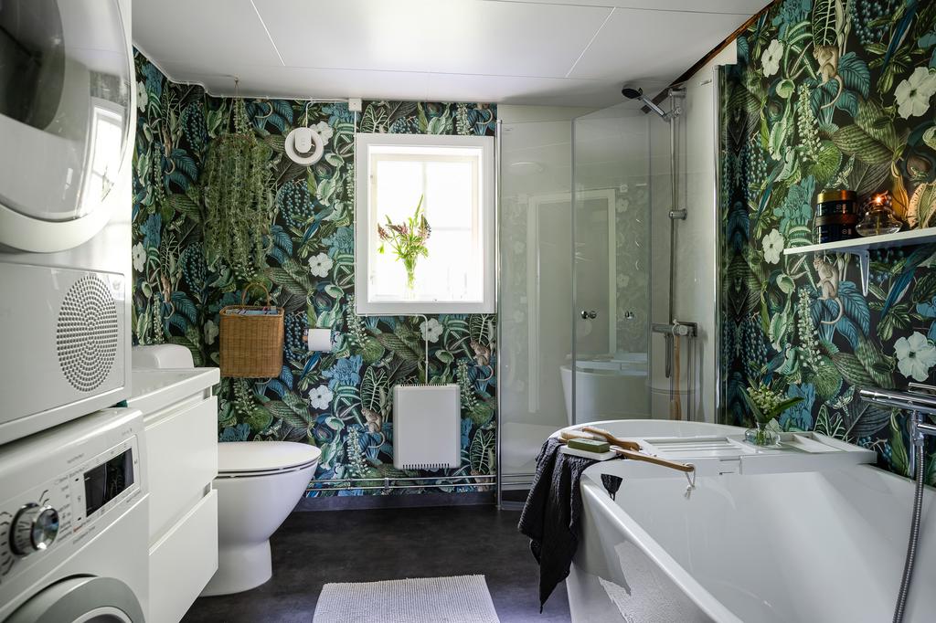 Badrummet är elegant inrett med mörkgrön, botaniskt inspirerad tapet som ger ett lyxigt och naturligt intryck. Här finns både badkar och dusch, stilrent handfat med underskåp samt klassiska detaljer som harmoniserar med husets lantliga stil.