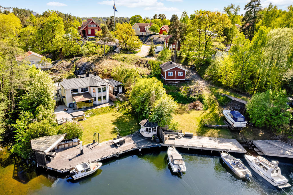 Samfälligheten sjötomt med brygga till höger i bild. I bakgrunden på höjden står huset