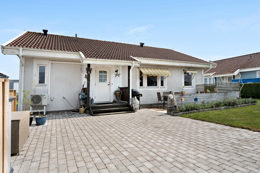 Framsidan på bostadshuset. Fint stenlagd gång mot huset & en härlig uteplats med kvällssol