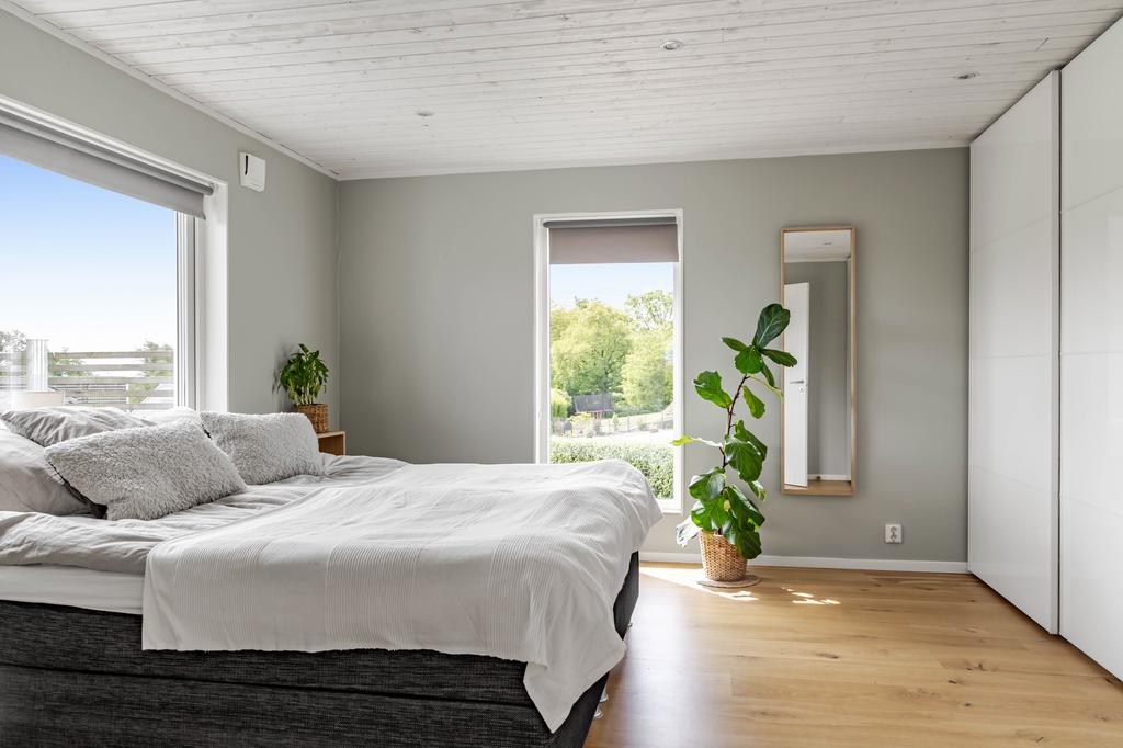 Rofyllt sovrum med plats för dubbelsäng, garderobsvägg och fint ljusinsläpp från två håll. Fönstren bjuder på grönskande utsikt och ger rummet en lugn känsla.