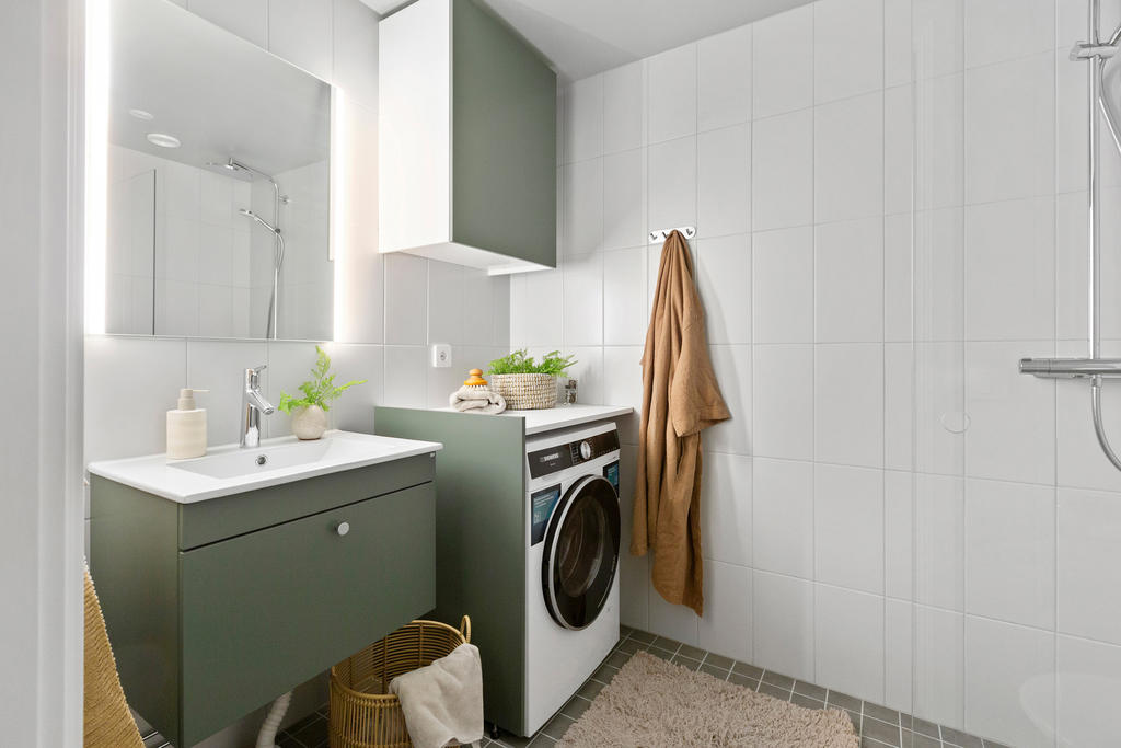 Helkaklat badrum med snygga grågröna luckor samt kombimaskin för tvätt/tork.