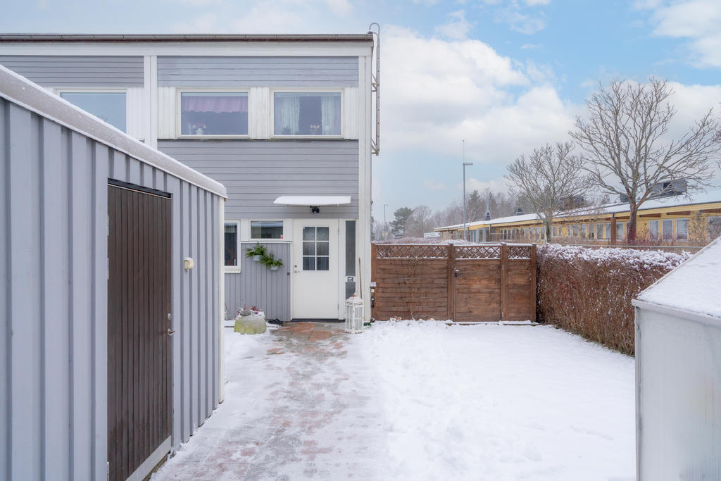 Delvis insynsskyddat tomt, förråd, gräsmatta och växthus på framsidan av huset. 