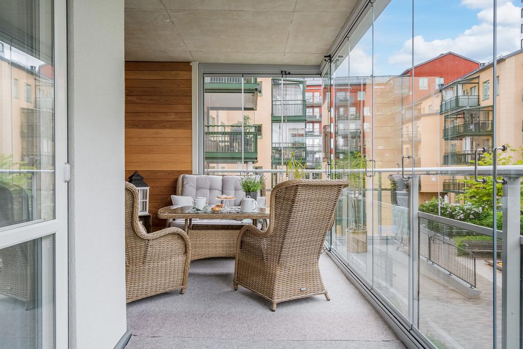 Stor inglasad balkong som vetter mot lummig innergård